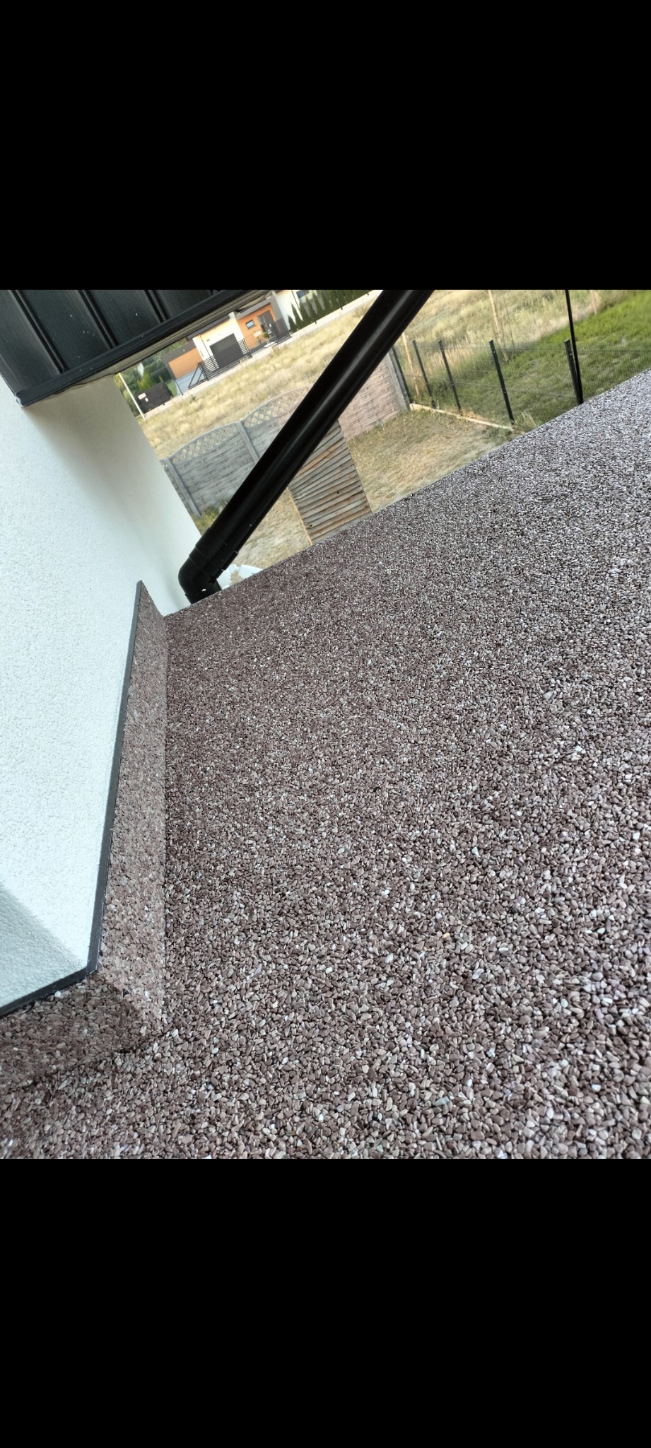 Wykończona powierzchnia balkonu z brązowego kruszywa kwarcowego, widoczna rynna odprowadzająca wodę i fragment elewacji budynku w tle.