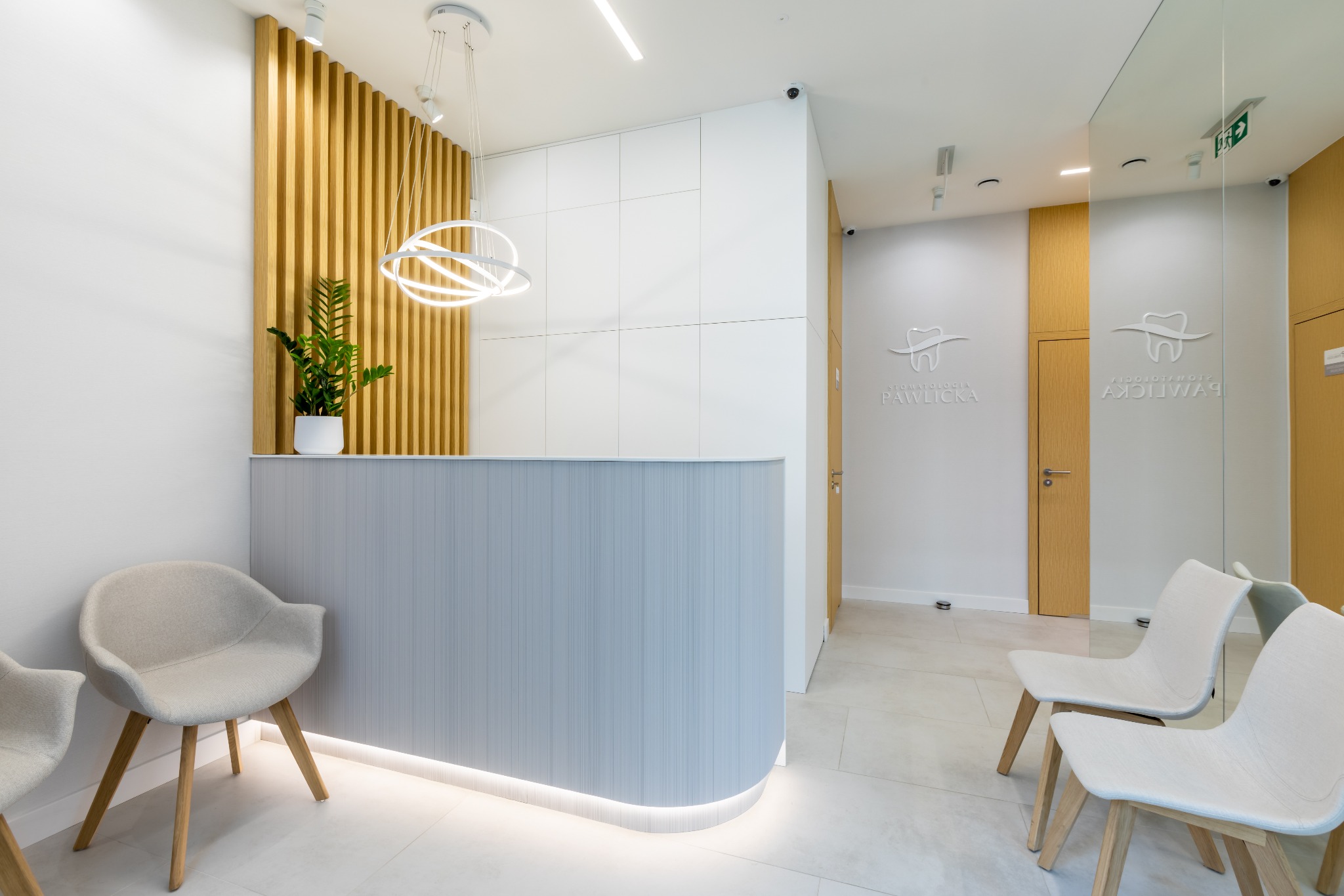 Jasne, nowoczesne wnętrze recepcji z szarym biurkiem, drewnianymi lamelami, okrągłą lampą i minimalistycznymi krzesłami w poczekalni, logo gabinetu na ścianie.