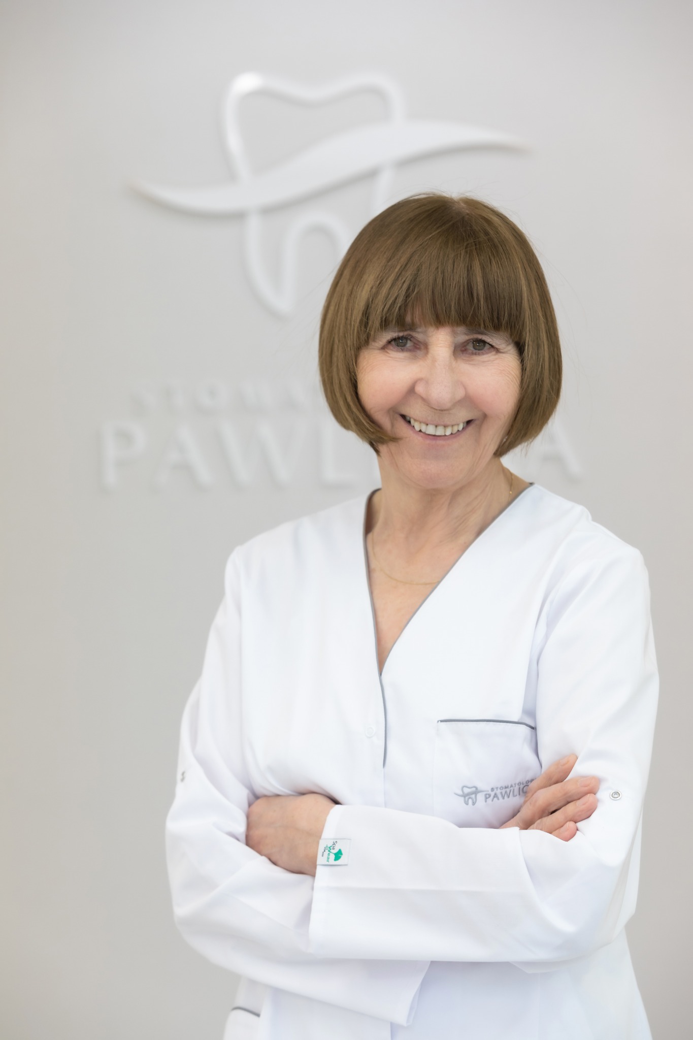 Uśmiechnięta lekarka w białym uniformie na tle ściany z logo gabinetu stomatologicznego