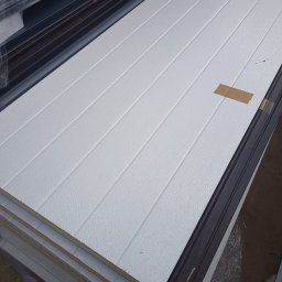 SESTAL SPÓŁKA CYWILNA JUSTYNA IBROM-JASIŃSKA, DAMIAN JASIŃSKI - Stos białych płyt warstwowych z widoczną strukturą powierzchni i brązową taśmą zabezpieczającą na jednej z nich.