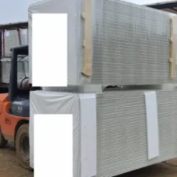 Wózek widłowy Toyota 50 SAS transportuje dwa zabezpieczone folią i drewnianymi listwami pakiety blachy trapezowej na terenie składu budowlanego.