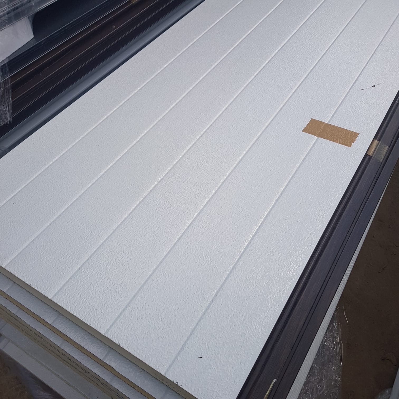 Stos białych płyt warstwowych z widoczną strukturą powierzchni i brązową taśmą zabezpieczającą na jednej z nich.