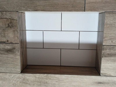 Wnęka w łazience wyłożona białymi, prostokątnymi płytkami, otoczona płytkami imitującymi drewno, widoczne fugi w kolorze szarym.