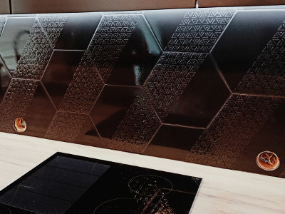 Ciemne, heksagonalne płytki z delikatnym wzorem trójkątów na ścianie nad kuchenką indukcyjną, widoczne otwory na instalacje