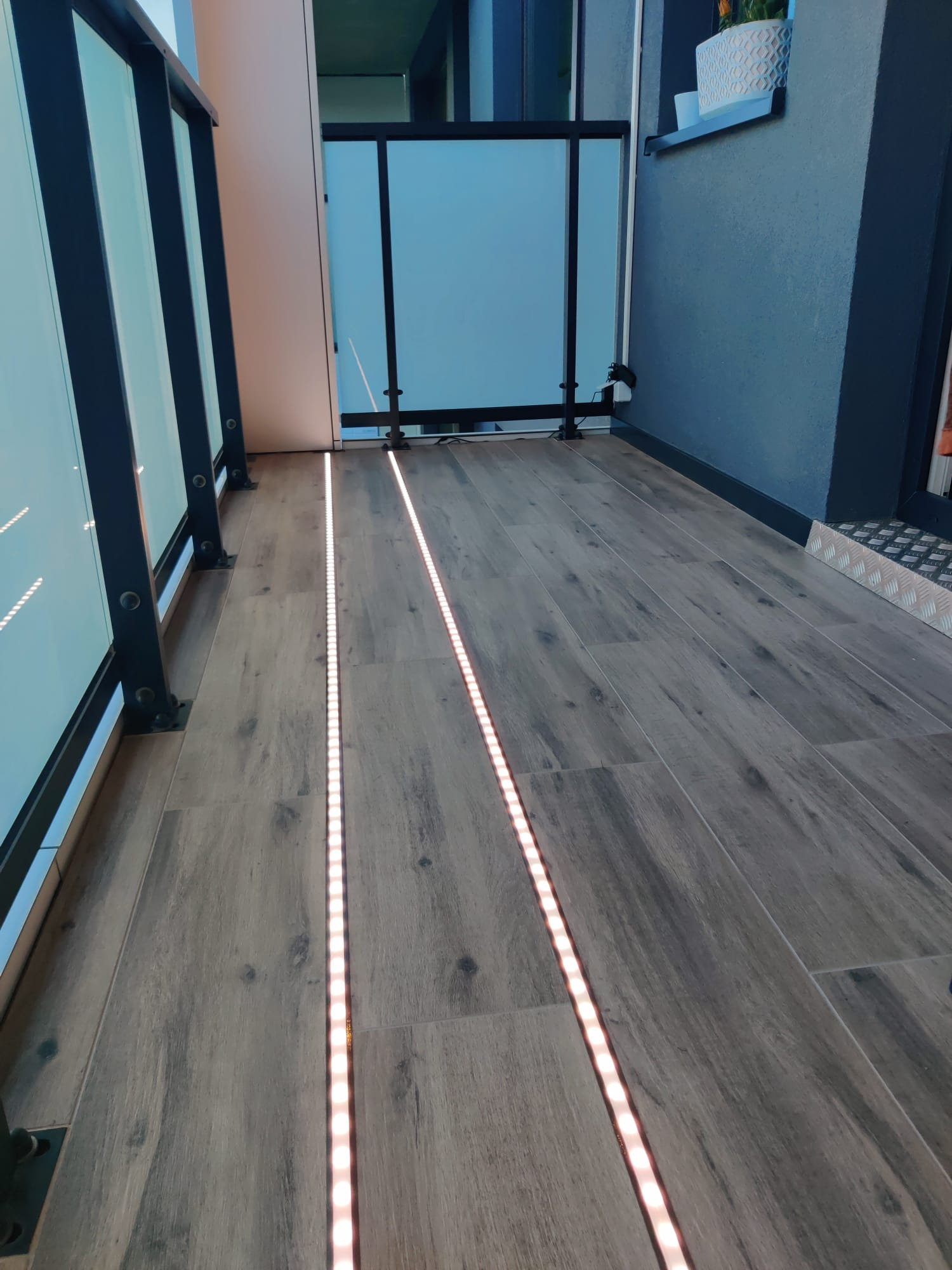 Balkon wyłożony płytkami imitującymi drewno z wbudowanym oświetleniem LED wzdłuż balustrady.