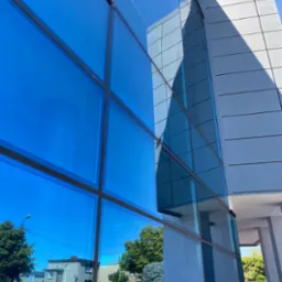 Błękitne, szklane elewacje biurowca w Krotoszynie odbijają krajobraz miasta i błękitne niebo, tworząc geometryczny wzór na fasadzie.