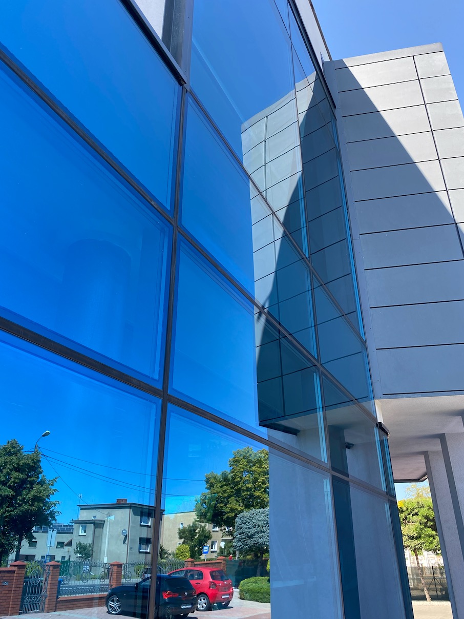 Błękitne, szklane elewacje biurowca w Krotoszynie odbijają krajobraz miasta i błękitne niebo, tworząc geometryczny wzór na fasadzie.