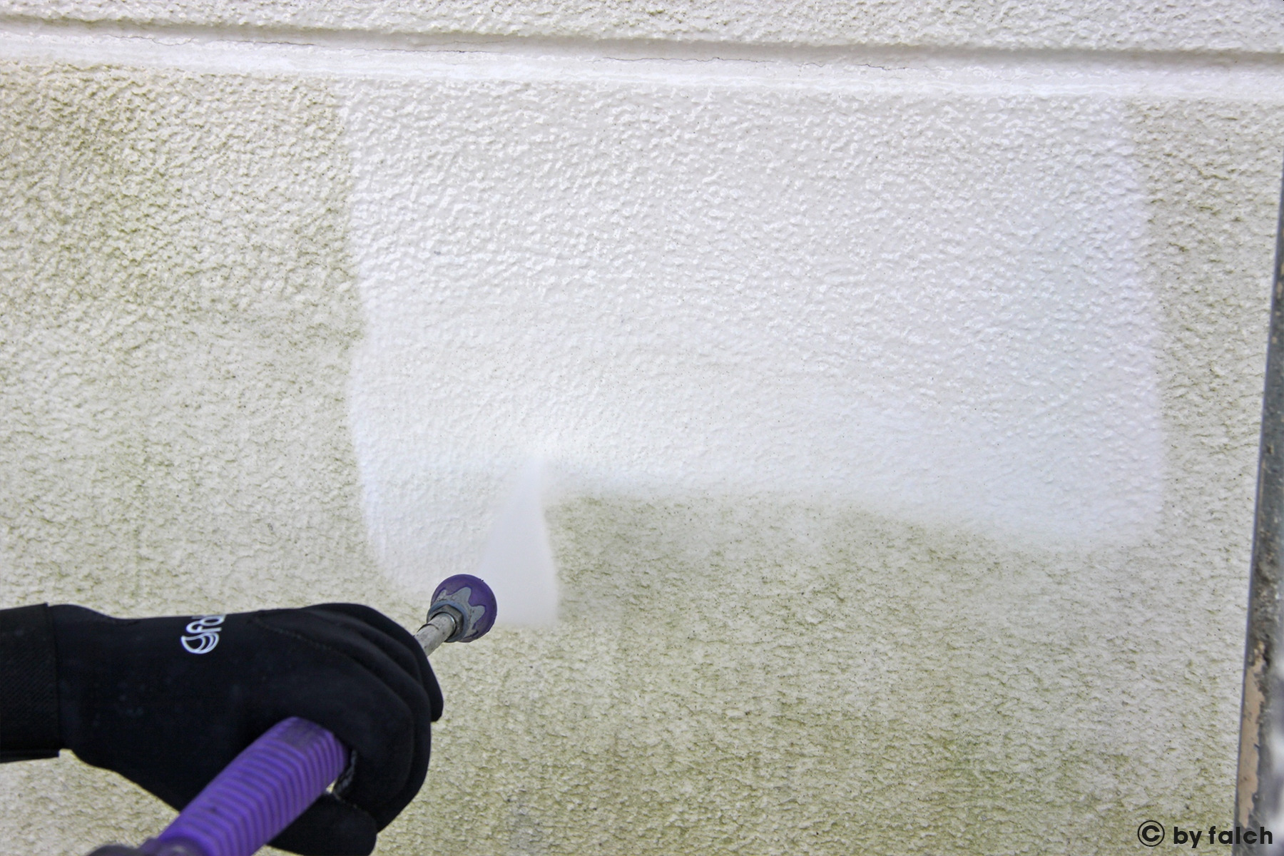 Czyszczenie elewacji budynku z zielonego nalotu za pomocą myjki ciśnieniowej, widoczna różnica między czystą a zabrudzoną powierzchnią.