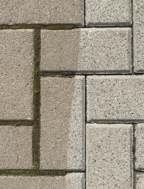 Częściowo oczyszczona szara kostka brukowa, widoczny kontrast między czystą i zabrudzoną powierzchnią, z zielonymi chwastami w spoinach.
