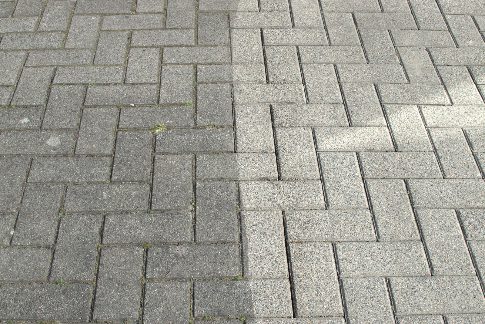 Fragment kostki brukowej ułożonej w jodełkę, widoczny kontrast pomiędzy wyczyszczoną, jaśniejszą prawą stroną a zabrudzoną, ciemniejszą lewą stroną.