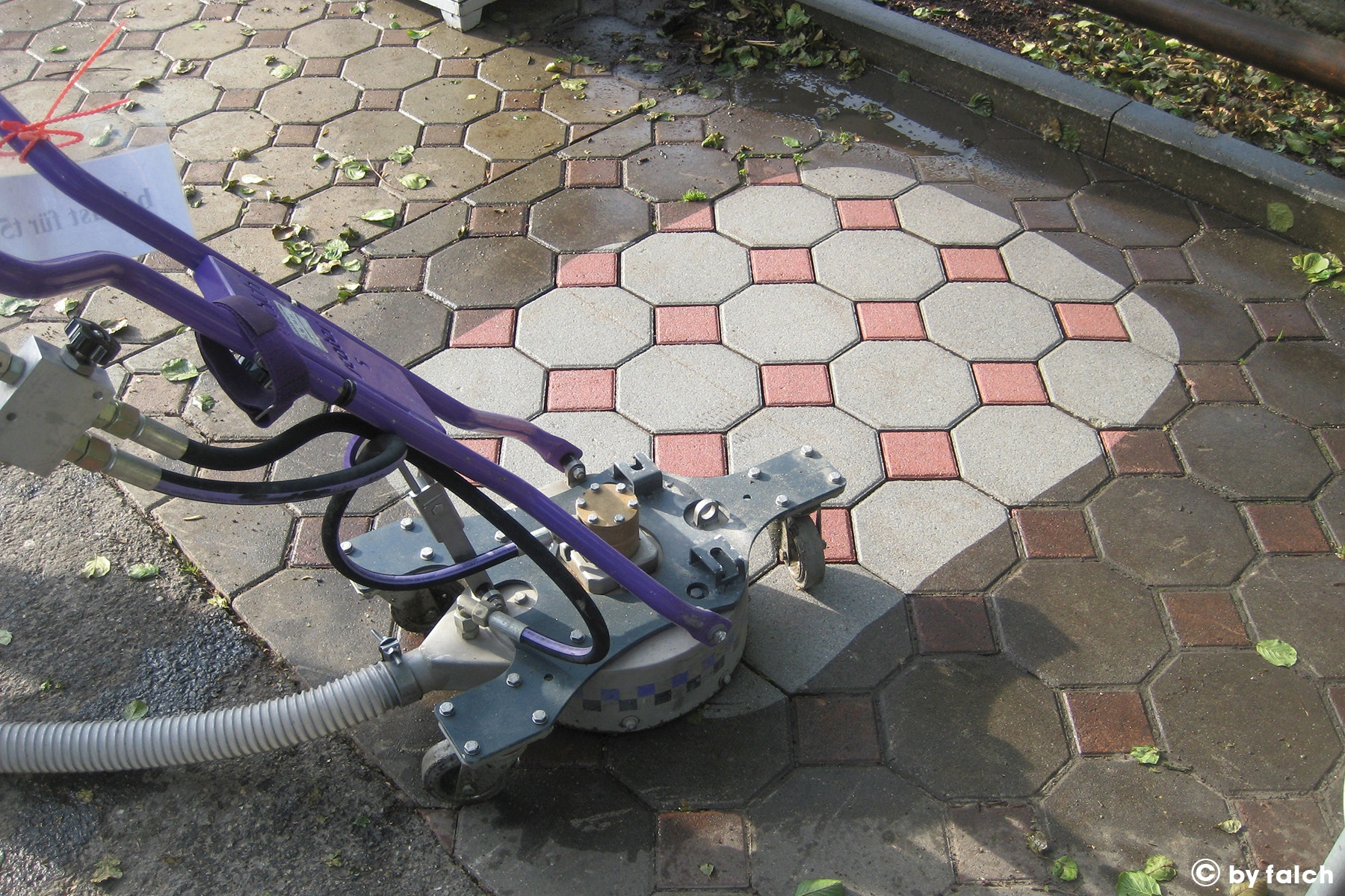 Profesjonalna maszyna do czyszczenia kostki brukowej z widocznym efektem czyszczenia - różnica między umytą a brudną powierzchnią kostki brukowej, wzór z szarych i czerwonych elementów.