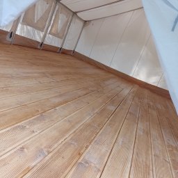 Sztuka Drewna Tworzymy z Pasją - Wnętrze namiotu z drewnianą podłogą z desek, widok z dołu w kierunku wejścia, białe płótno namiotu z widocznymi oknami.