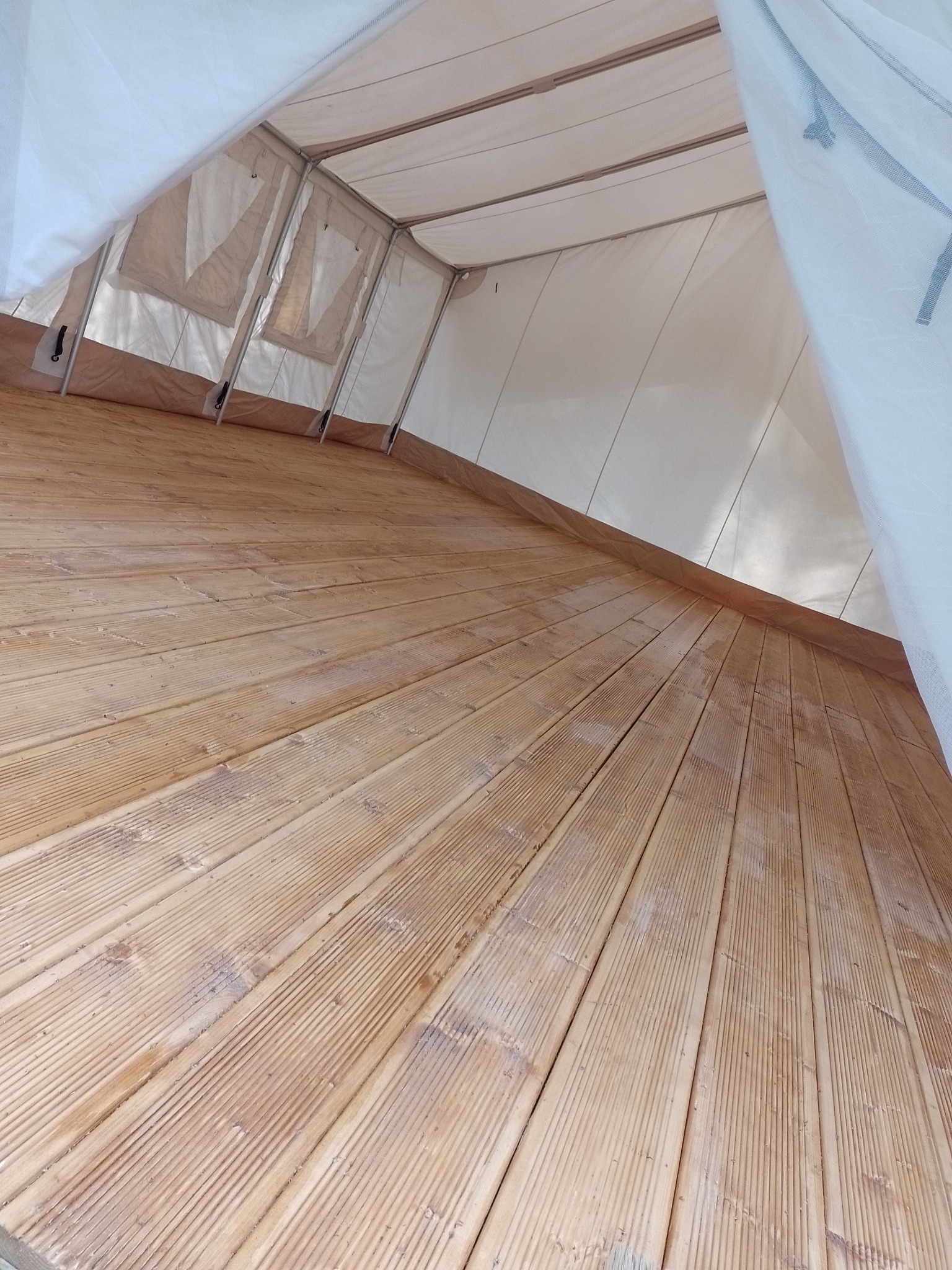 Wnętrze namiotu z drewnianą podłogą z desek, widok z dołu w kierunku wejścia, białe płótno namiotu z widocznymi oknami.