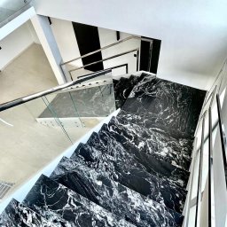 Abikam Halina Wilczyńska - Nowoczesne schody kamienne z czarnego marmuru z białymi żyłami, widok z góry, szklana balustrada, minimalistyczny design wnętrza.