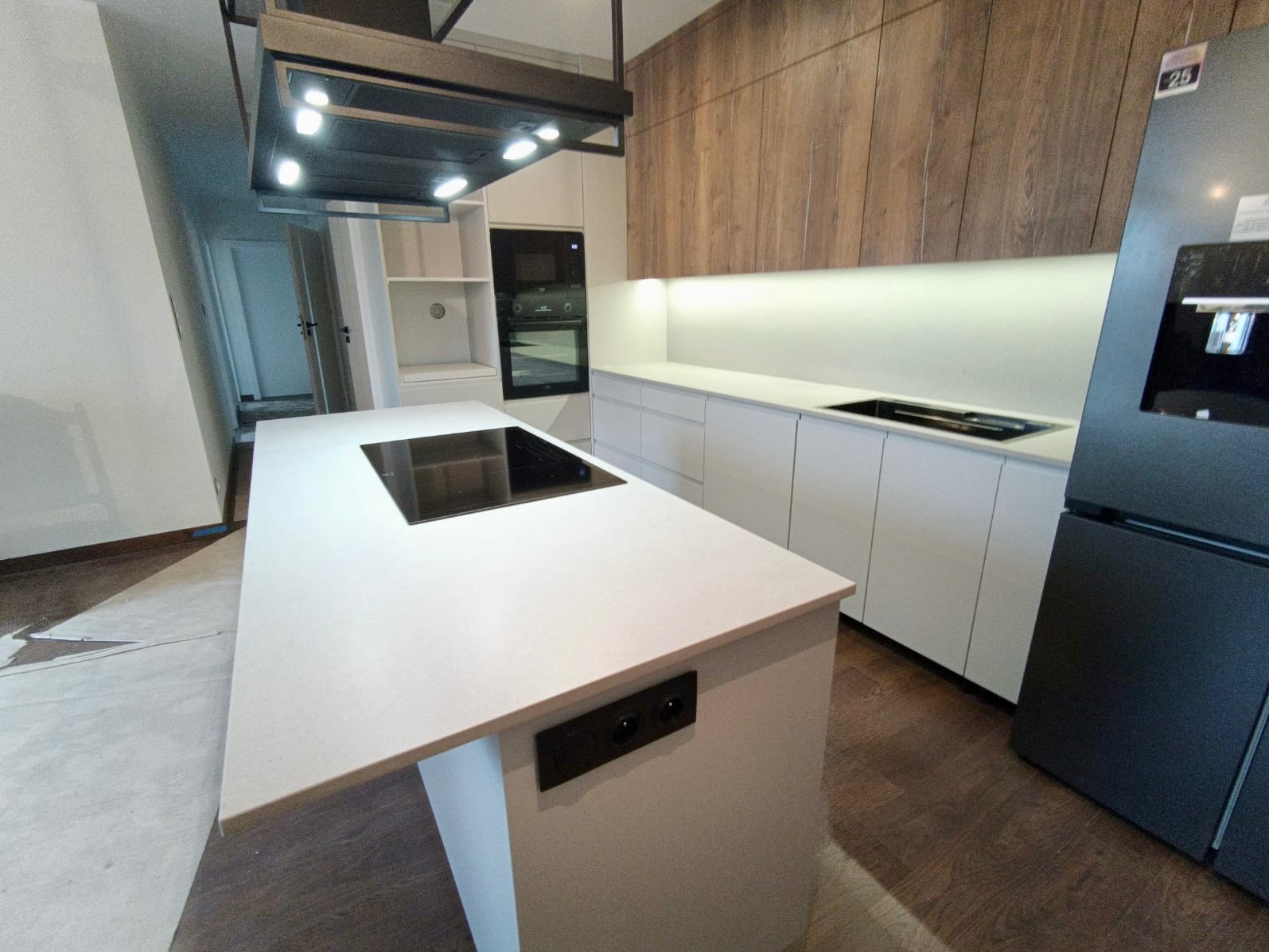 Nowoczesna kuchnia z wyspą i blatem z jasnego kamienia, wbudowana płyta indukcyjna, drewniane szafki wiszące, oświetlenie LED pod szafkami, minimalistyczny design.