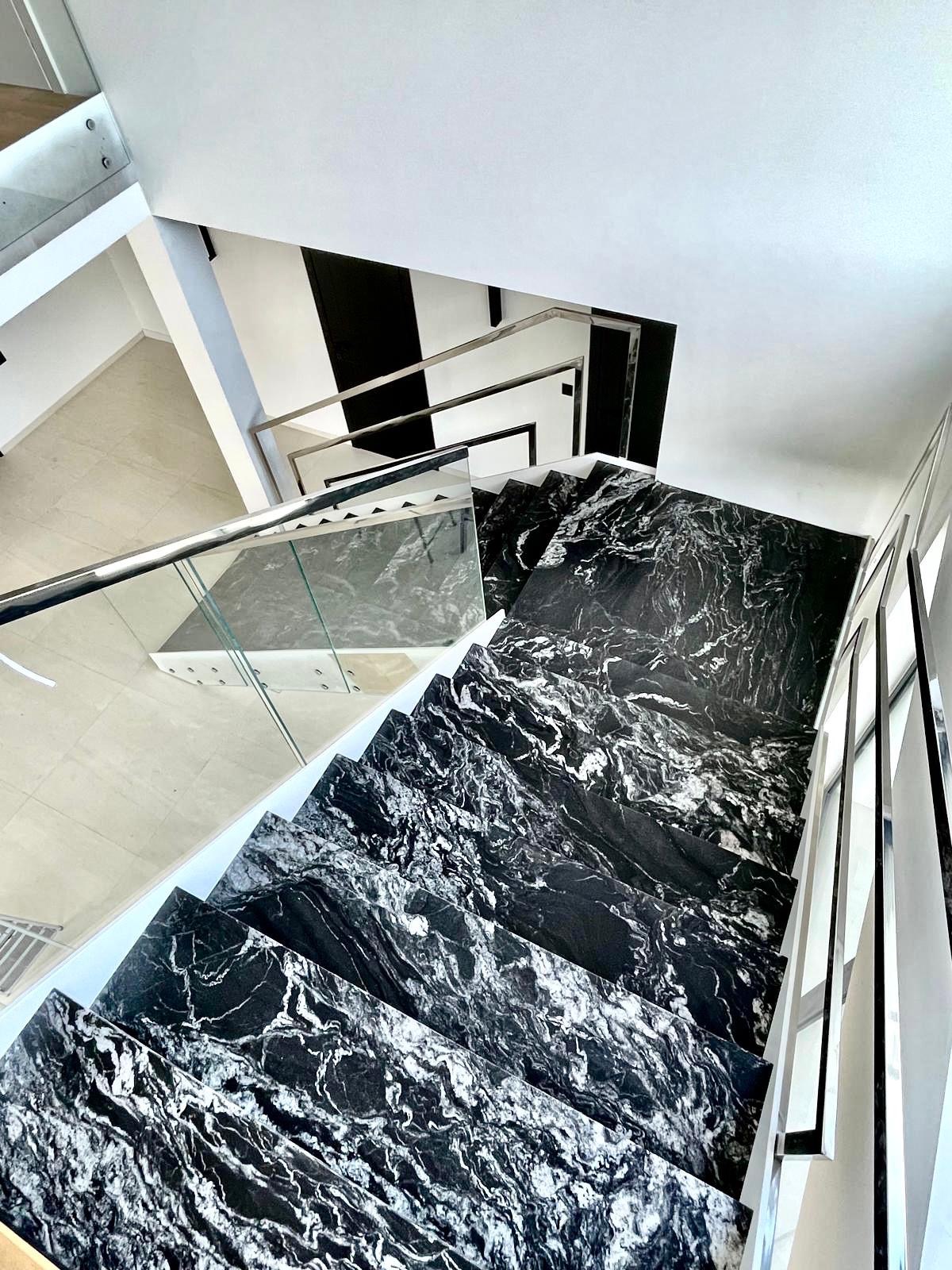 Nowoczesne schody kamienne z czarnego marmuru z białymi żyłami, widok z góry, szklana balustrada, minimalistyczny design wnętrza.
