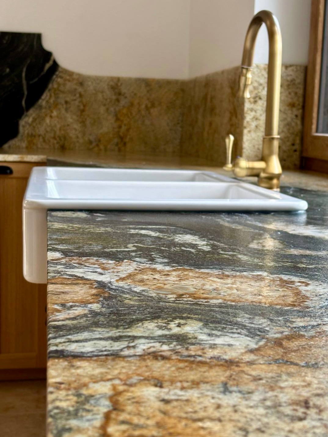 Błyszczący blat kamienny z umywalką farmerską i złotą baterią, ukazujący unikalny wzór kamienia w odcieniach brązu, szarości i bieli. Widok z bliska na wykończony detal.