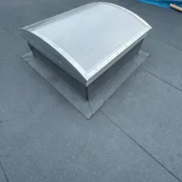 Nowo zainstalowany świetlik dachowy na płaskim dachu pokrytym papą, widoczne uszczelnienia i brak zabrudzeń.