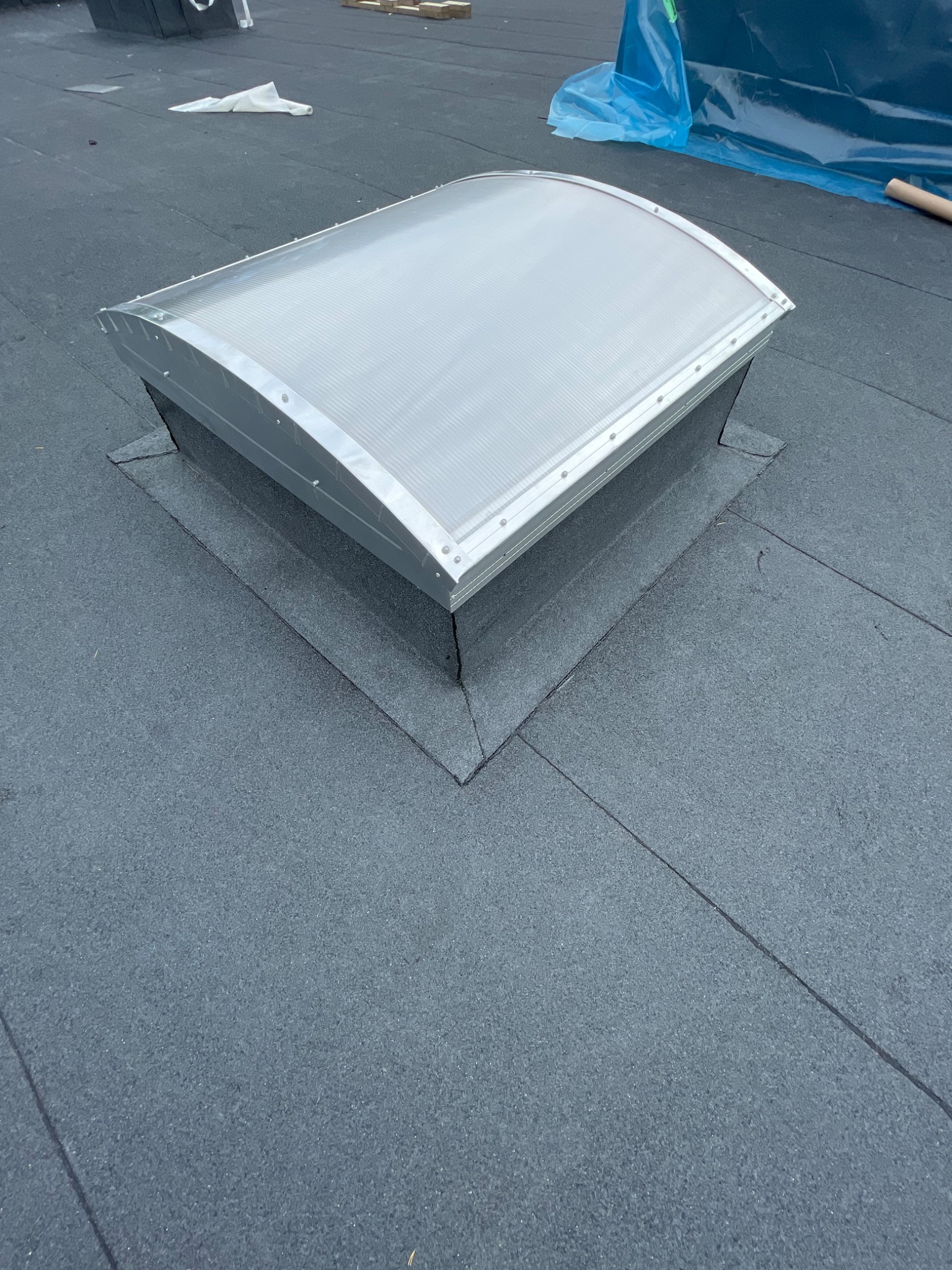 Nowo zainstalowany świetlik dachowy na płaskim dachu pokrytym papą, widoczne uszczelnienia i brak zabrudzeń.