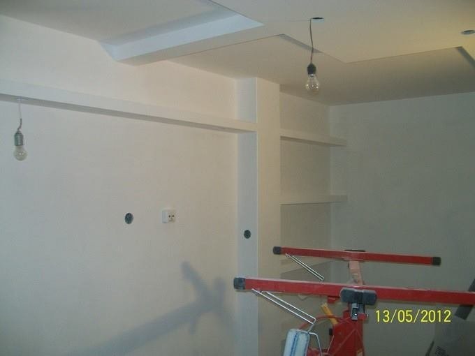 Wnętrze w trakcie malowania na biało, widoczne niedokończone sufity podwieszane, gołe żarówki zwisające z sufitu i czerwony stojak malarski.