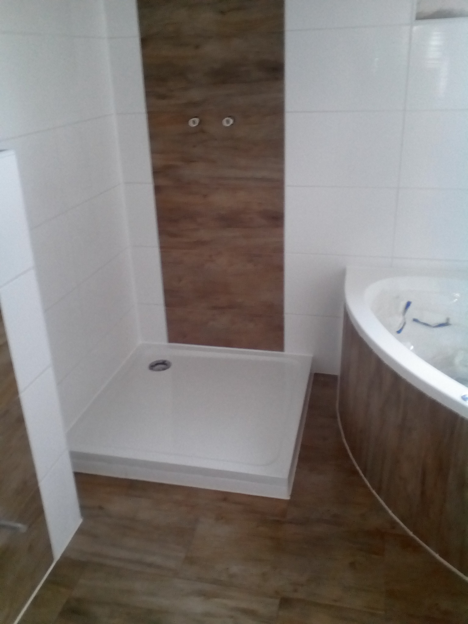 Nowoczesna łazienka z białymi płytkami, kabiną prysznicową z odpływem liniowym i wanną z hydromasażem, wykończona panelami imitującymi drewno na ścianie i podłodze.