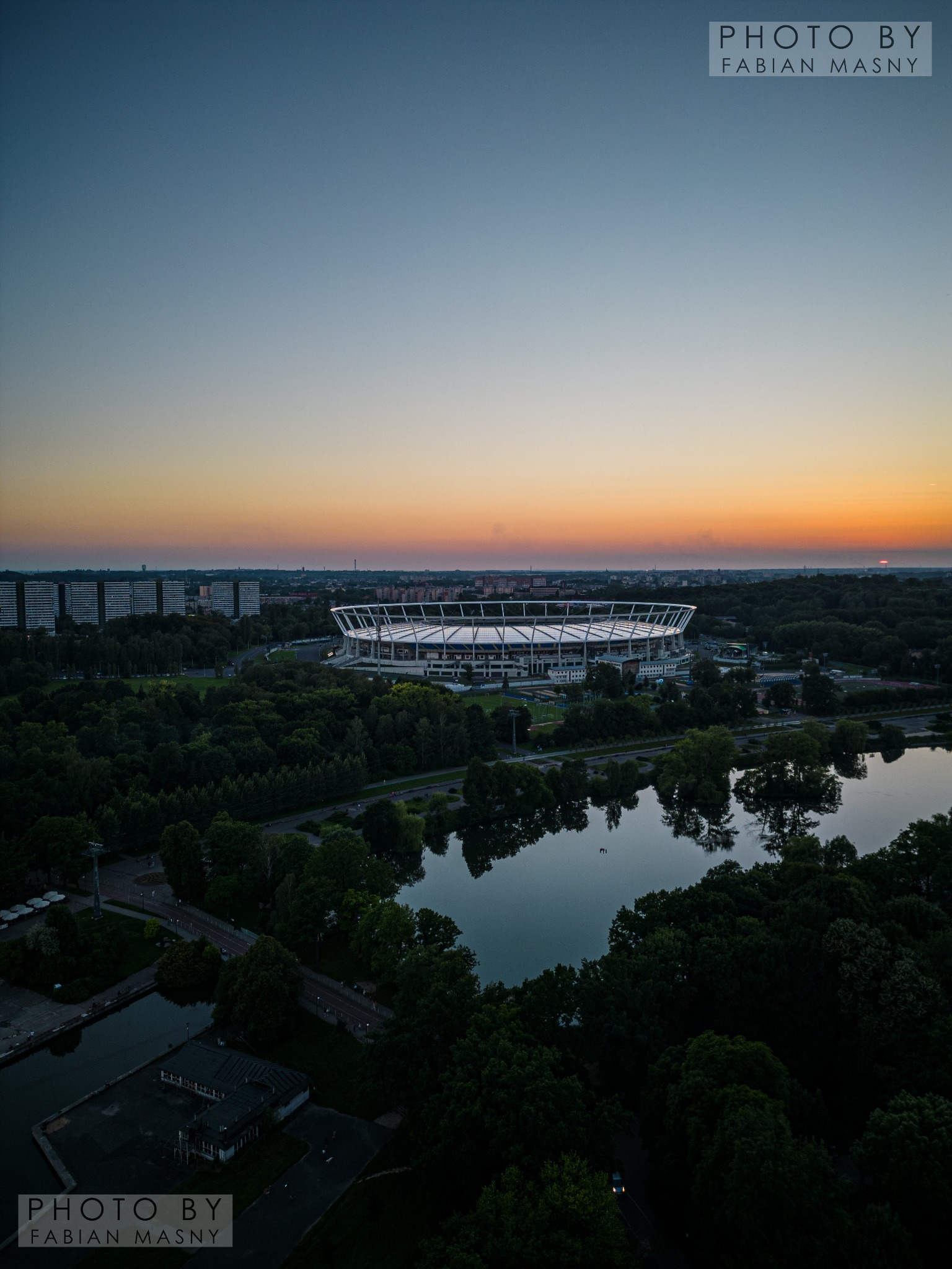 Panorama Warszawy o zmierzchu z widokiem na Stadion Narodowy, park, jezioro i budynki mieszkalne.