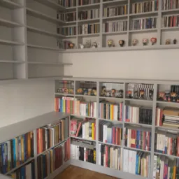 Szara, zabudowana biblioteczka od podłogi do sufitu, wypełniona książkami, płytami CD i figurkami kolekcjonerskimi, z parkietem na podłodze.