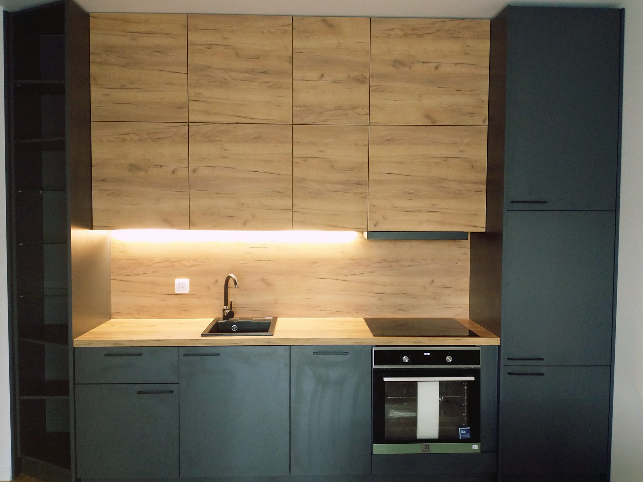 Nowoczesna kuchnia w odcieniach szarości i drewna, z podświetlanym blatem i minimalistycznym zlewem.