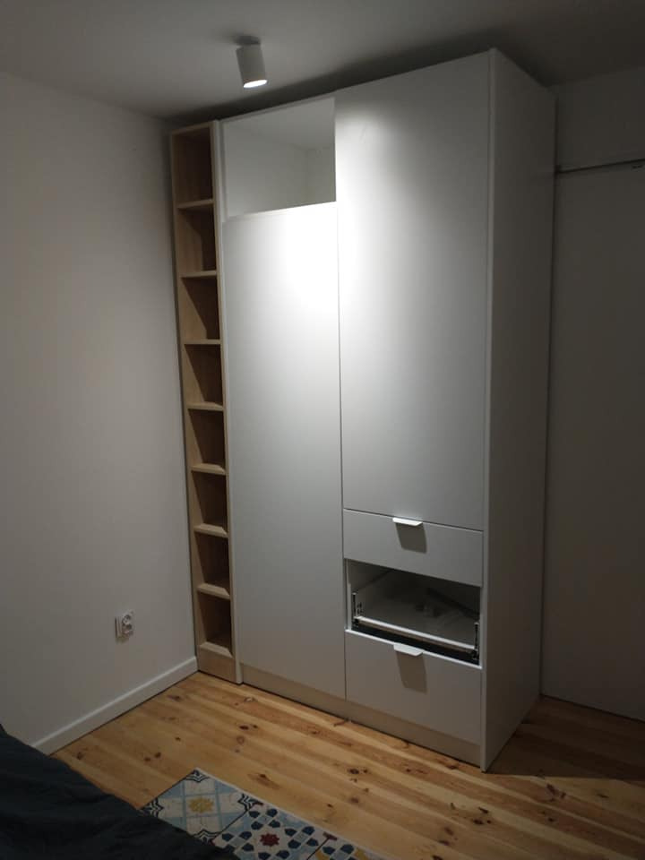 Biała szafa wnękowa z szufladami i otwartym regałem z jasnego drewna, widok z poziomu podłogi na parkiet w pokoju.