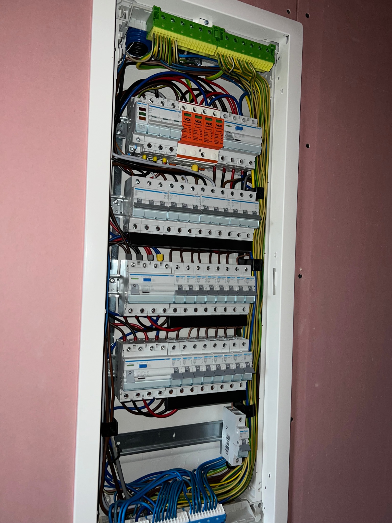 Rozdzielnica elektryczna z zainstalowanymi bezpiecznikami, zabezpieczeniami przepięciowymi i listwami zaciskowymi, widoczne przewody w różnych kolorach, zamontowana w ścianie z płyt...