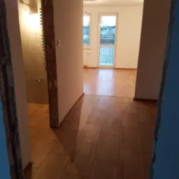 Wnętrze mieszkania w trakcie remontu: widok na wykończoną podłogę z płytek imitujących drewno, surową łazienkę z widocznymi instalacjami i odnowiony pokój z parkietem i białymi ścianami.