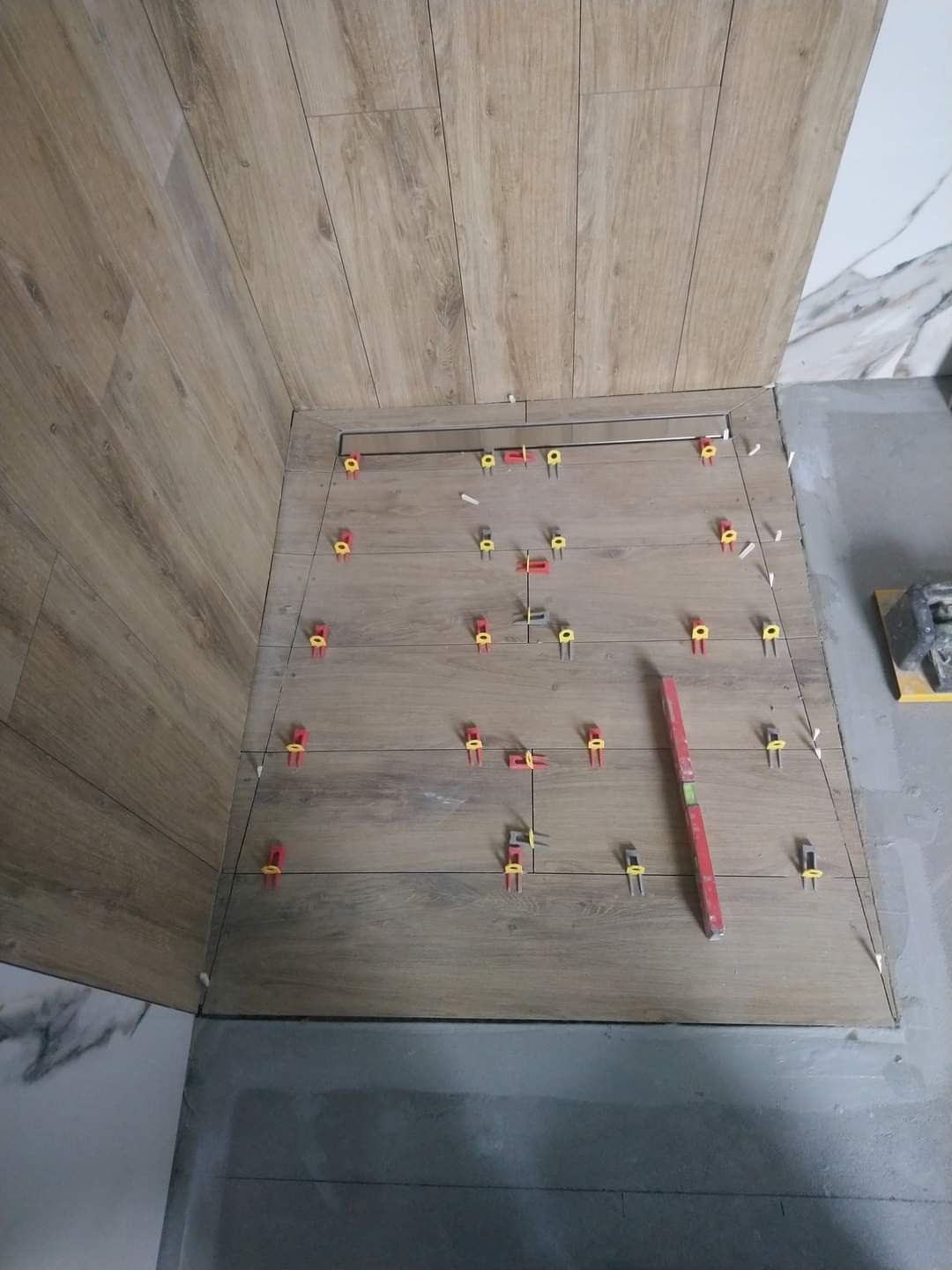 Układanie płytek imitujących drewno w kabinie prysznicowej, z widocznymi krzyżykami dystansowymi i poziomicą, podkreślającymi precyzję montażu.