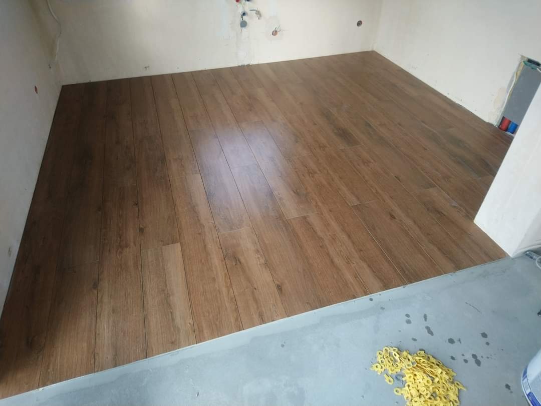 Ułożona podłoga z paneli imitujących drewno w trakcie prac wykończeniowych, widoczne niedoskonałości ścian i resztki po budowie.