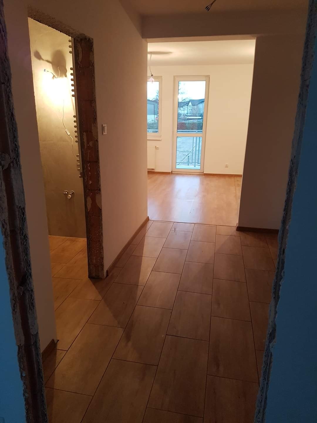 Wnętrze mieszkania w trakcie remontu: widok na wykończoną podłogę z płytek imitujących drewno, surową łazienkę z widocznymi instalacjami i odnowiony pokój z parkietem i białymi ścianami.