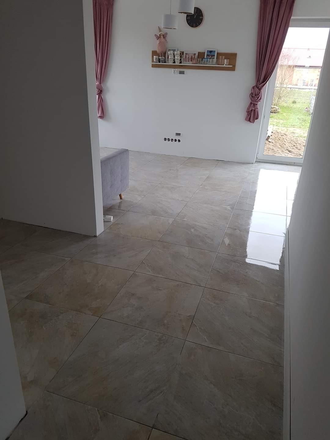 Beżowe płytki podłogowe ułożone w kwadraty w nowym, jasnym pokoju z różowymi zasłonami, widok z korytarza.