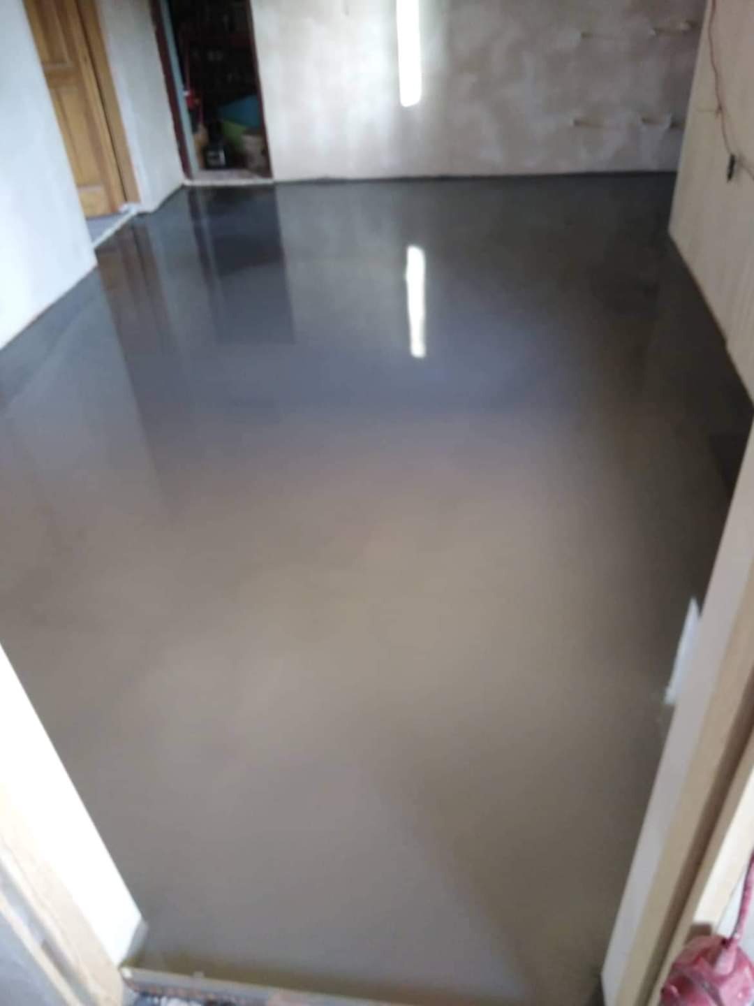 Wylany, mokry samopoziomujący podkład podłogowy w jasnym pomieszczeniu z otwartymi drzwiami w tle.