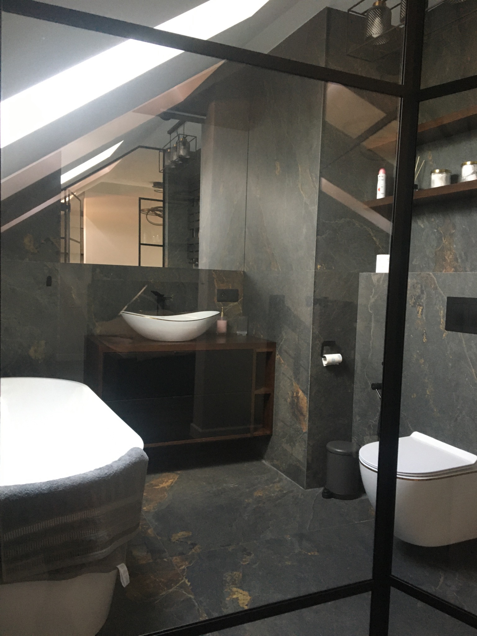 Nowoczesna łazienka z kabiną prysznicową typu walk-in, umywalką nablatową, toaletą podwieszaną i marmurowymi płytkami w odcieniach szarości i złota.