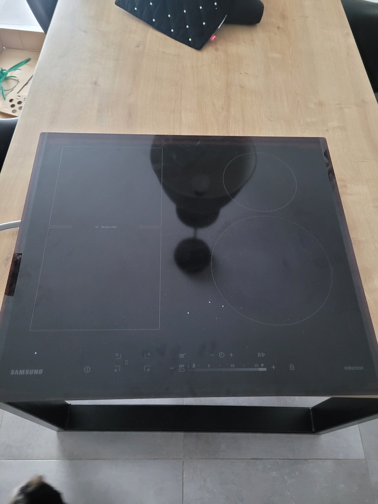 Czarna płyta indukcyjna marki Samsung umieszczona na drewnianym blacie, widoczne cztery pola grzewcze, panel sterowania dotykowy z suwakiem temperatury i oznaczeniami funkcji.