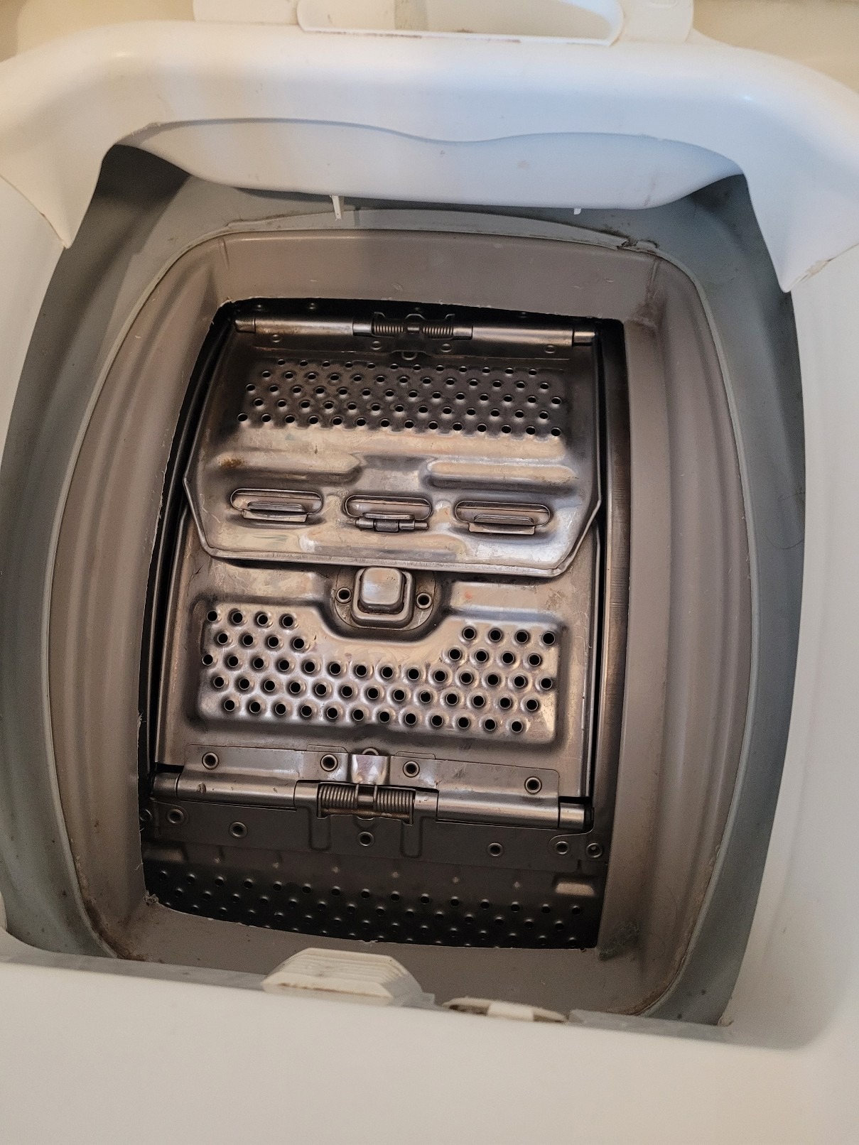 Wnętrze pralki automatycznej z otwartymi drzwiczkami bębna, widoczne ślady użytkowania i osad na metalowych elementach.