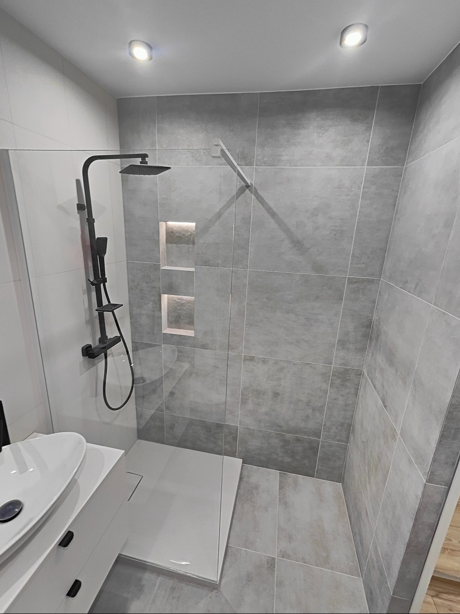 Nowoczesna kabina prysznicowa z szarymi płytkami, czarną armaturą i wnękami z oświetleniem LED.