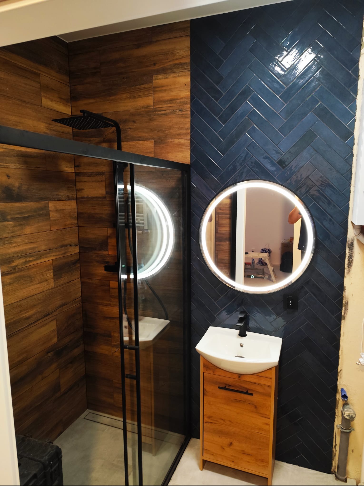 Wykończona łazienka w stylu nowoczesnym: kabina prysznicowa z czarną armaturą i odpływem liniowym, drewnopodobne płytki na ścianie, niebieskie płytki ułożone w jodełkę, okrągłe lustro...