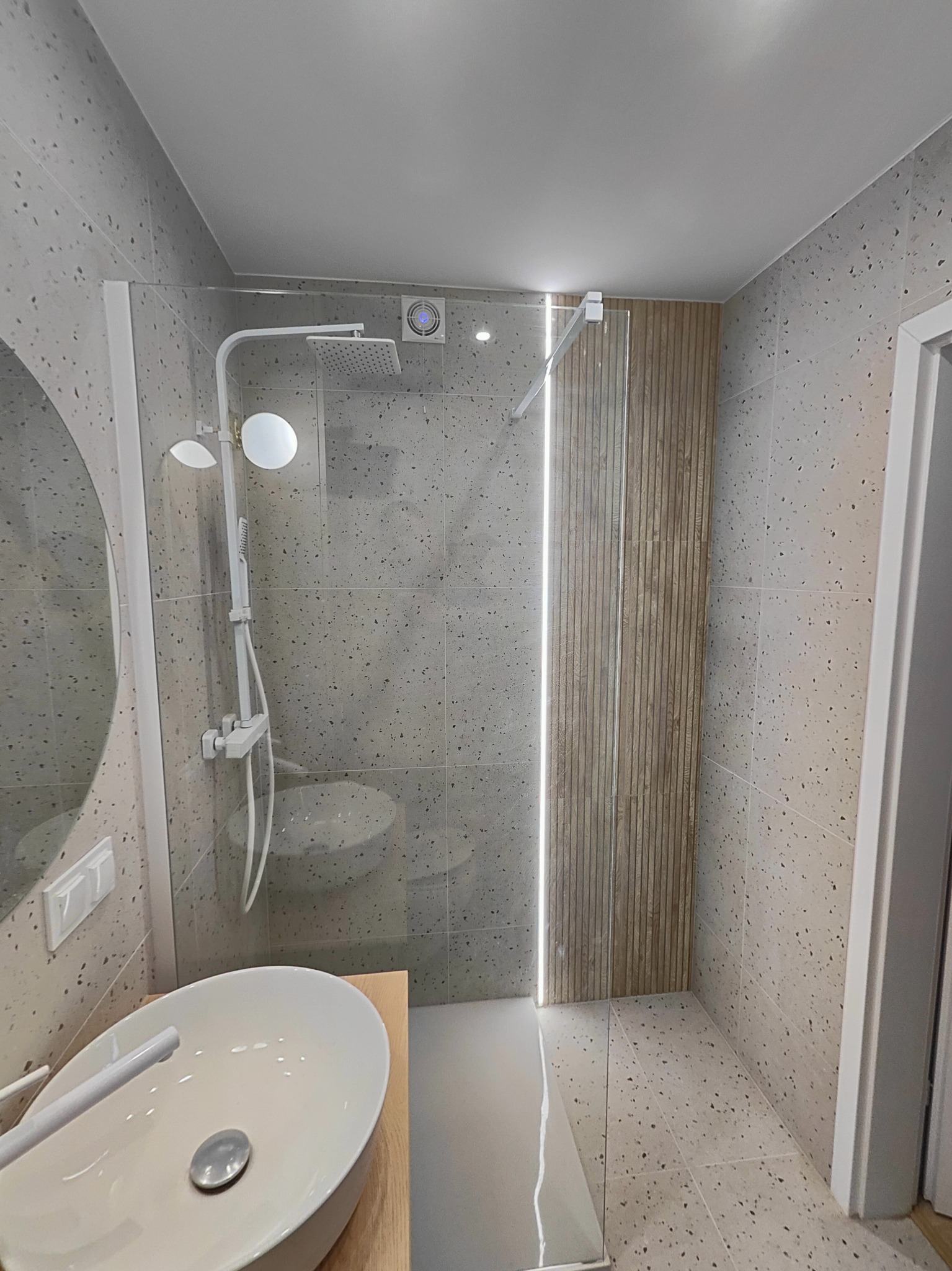 Nowoczesna łazienka z kabiną prysznicową typu walk-in, umywalką nablatową i szarymi płytkami lastryko na ścianach i podłodze. Kabina prysznicowa ze szklaną ścianą i drewnianą ścianką...