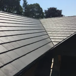 Nowe, grafitowe dachówki ułożone na dachu, widoczne drzewa w tle.