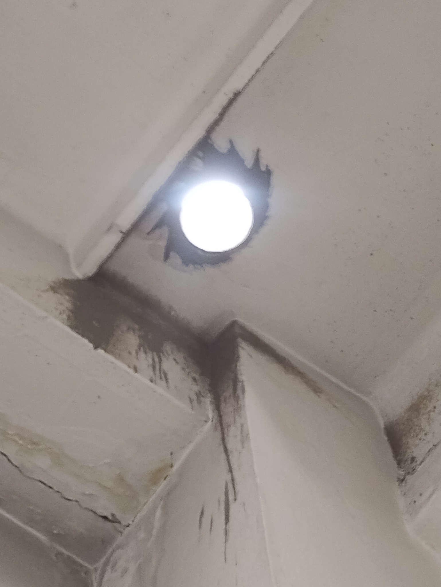 Otwór w suficie z widocznymi zaciekami i śladami wilgoci wokół, prawdopodobnie po nieszczelności dachu.