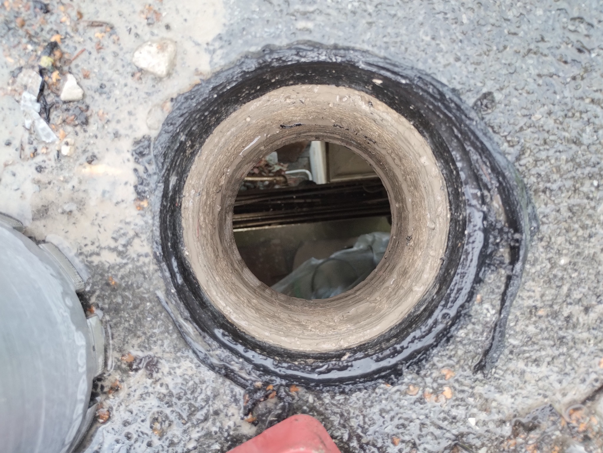 Otwór kanalizacyjny z widocznymi śladami uszczelniania, otoczony gruzem i wilgotnym betonem.