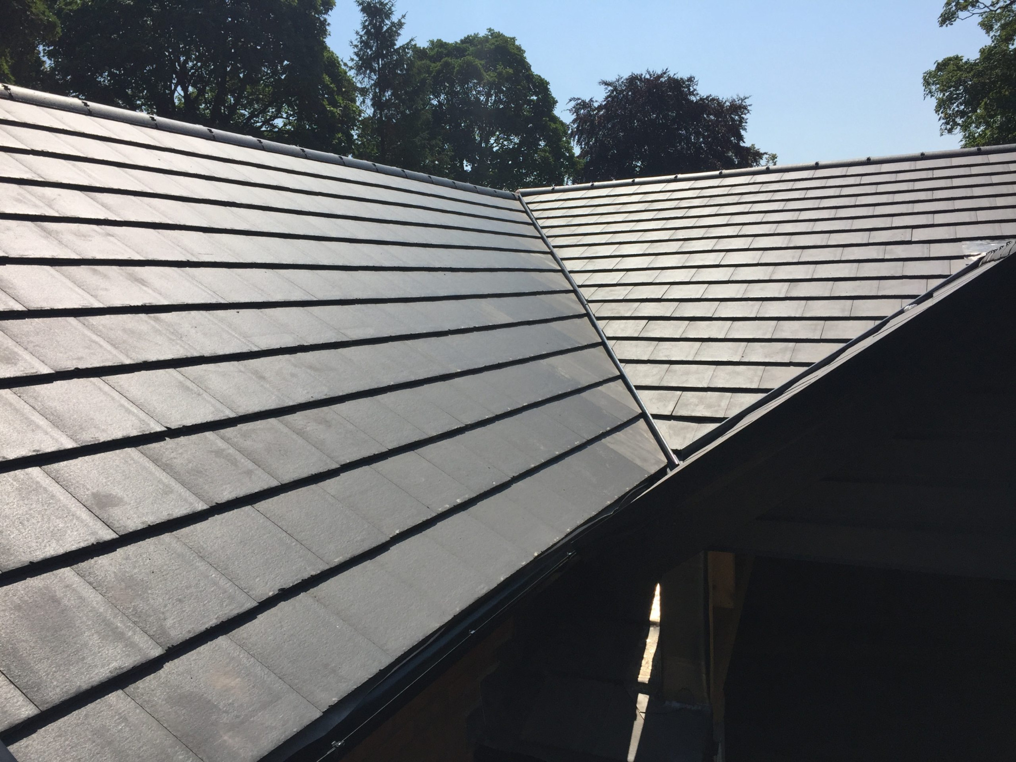 Nowe, grafitowe dachówki ułożone na dachu, widoczne drzewa w tle.