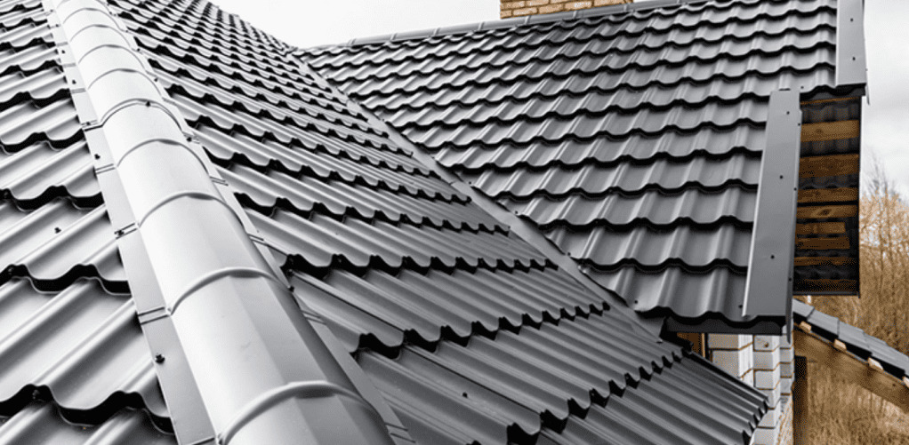 Nowoczesne pokrycie dachu z blachodachówki w kolorze grafitowym, widoczne orynnowanie i detale wykończeniowe przy kominie z cegły klinkierowej.