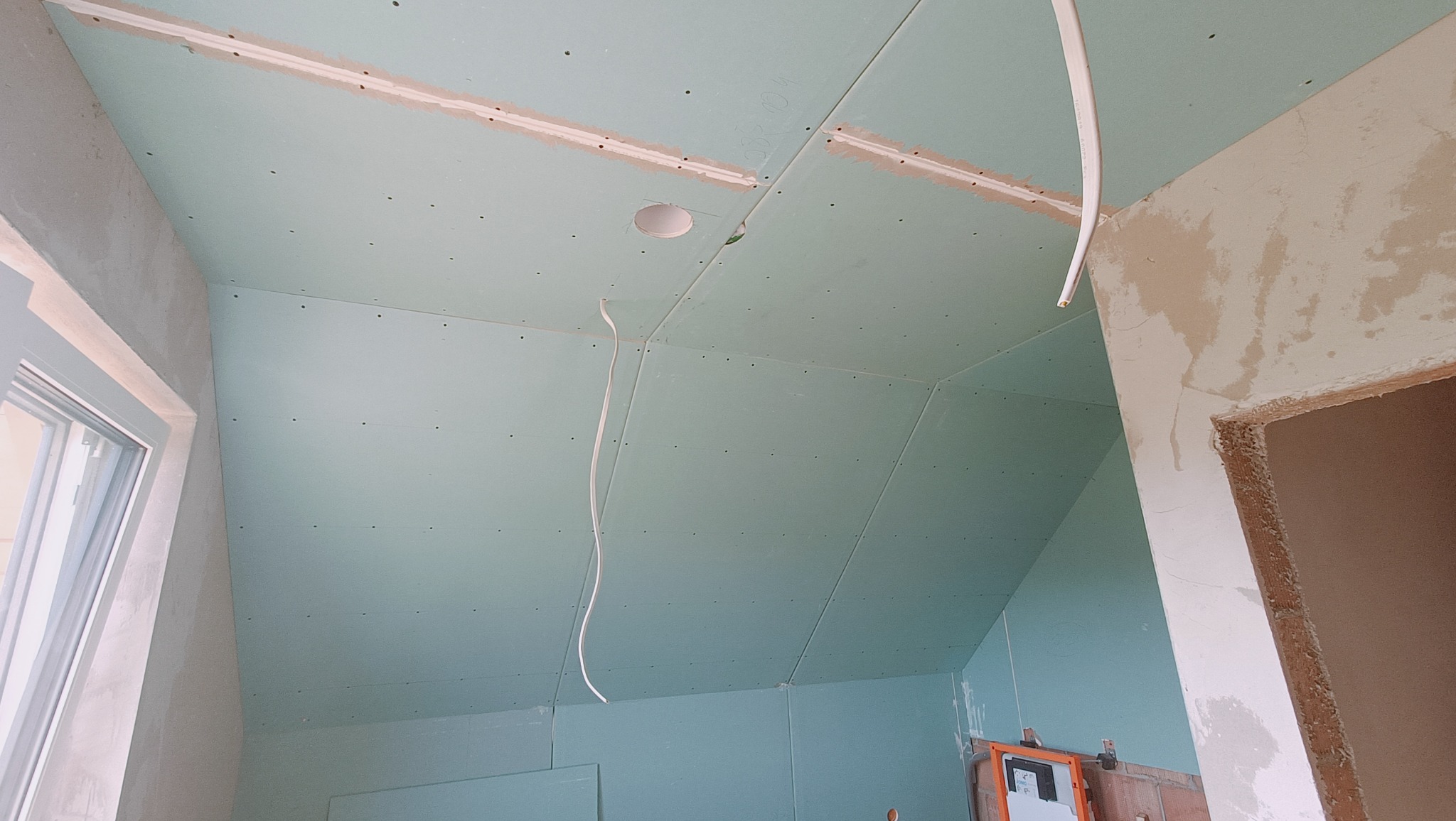 Poddasze z ukończonym montażem płyt karton-gips, widoczne otwory na oświetlenie i wystające przewody elektryczne, ślady szpachlowania na łączeniach płyt.