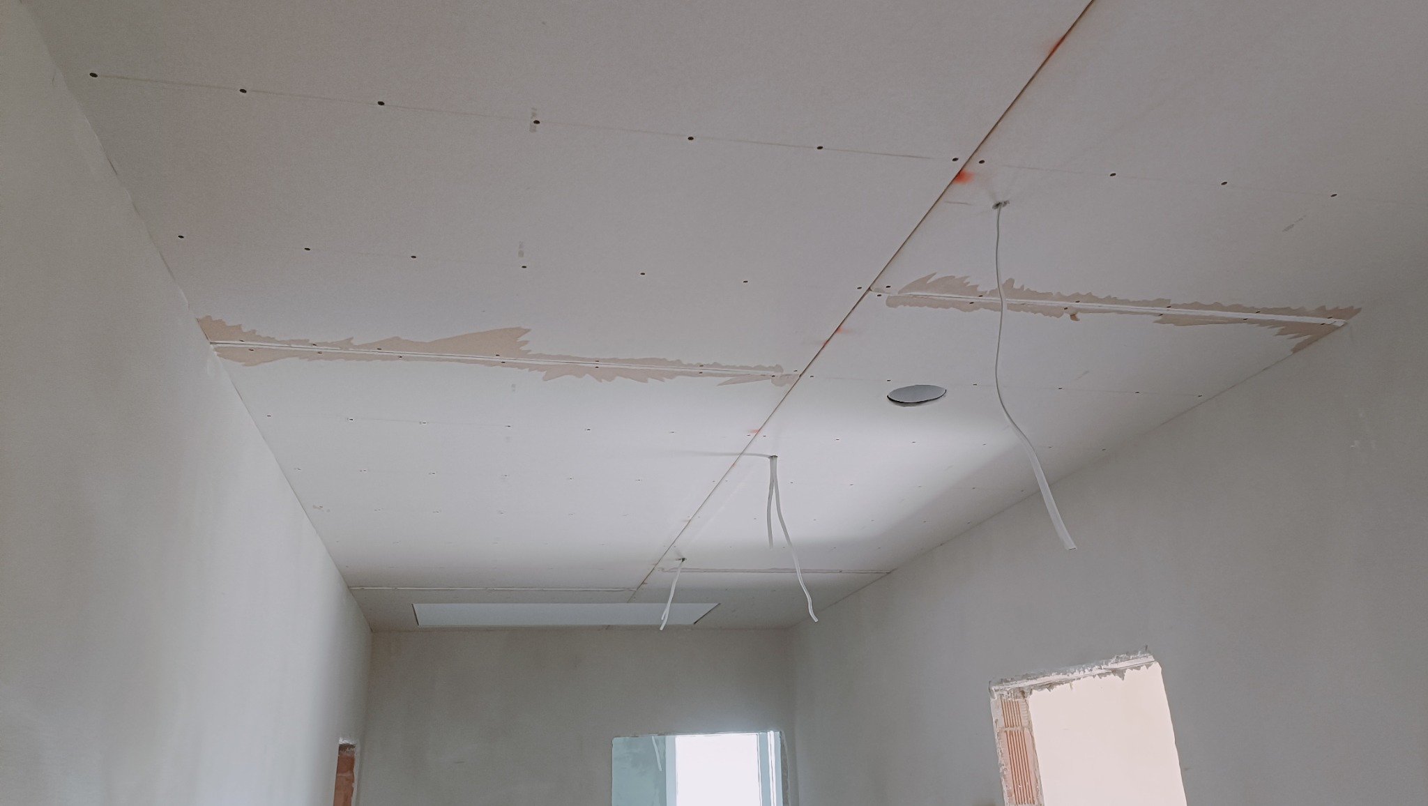 Montaż sufitu podwieszanego z widocznymi łączeniami płyt i wystającymi przewodami elektrycznymi przed szpachlowaniem.