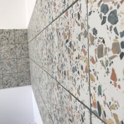 Snihur Volodymyr - Ściana wyłożona płytkami imitującymi lastryko z widoczną fugą, fragment drabiny malarskiej w tle.